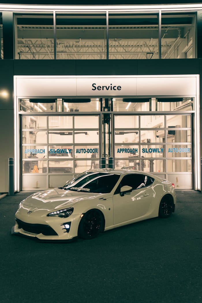 A white sports car parked outside a modern service center at night, highlighting elegance and automotive style.